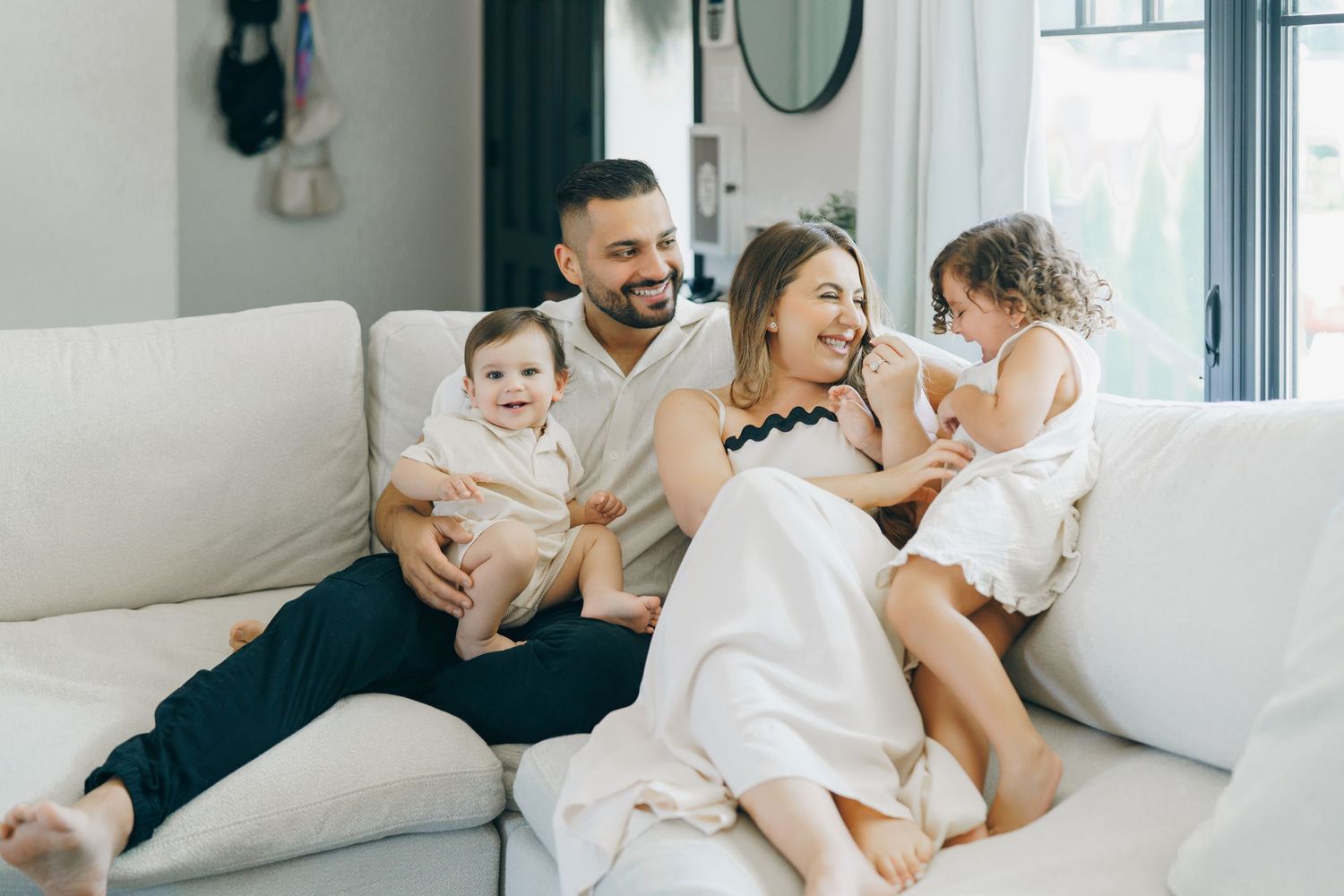 Happy family of four laughing together on a white sofa in a bright modern living room.