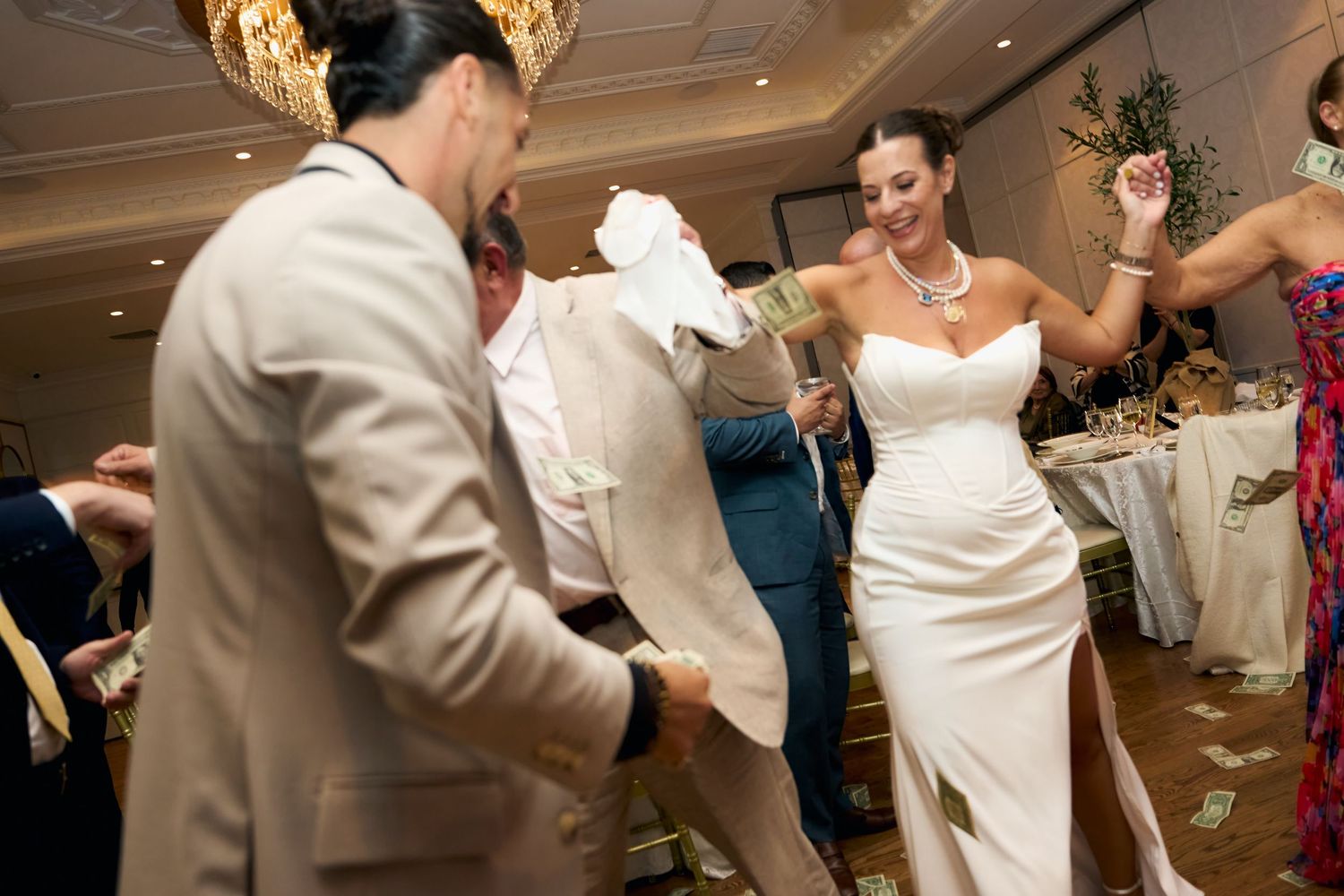 Bride in white gown and groom in tan suit dancing joyfully at elegant wedding reception.
