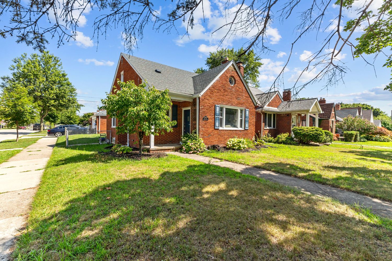 Charming red brick cottage with mature trees, green lawn, and classic architectural details.