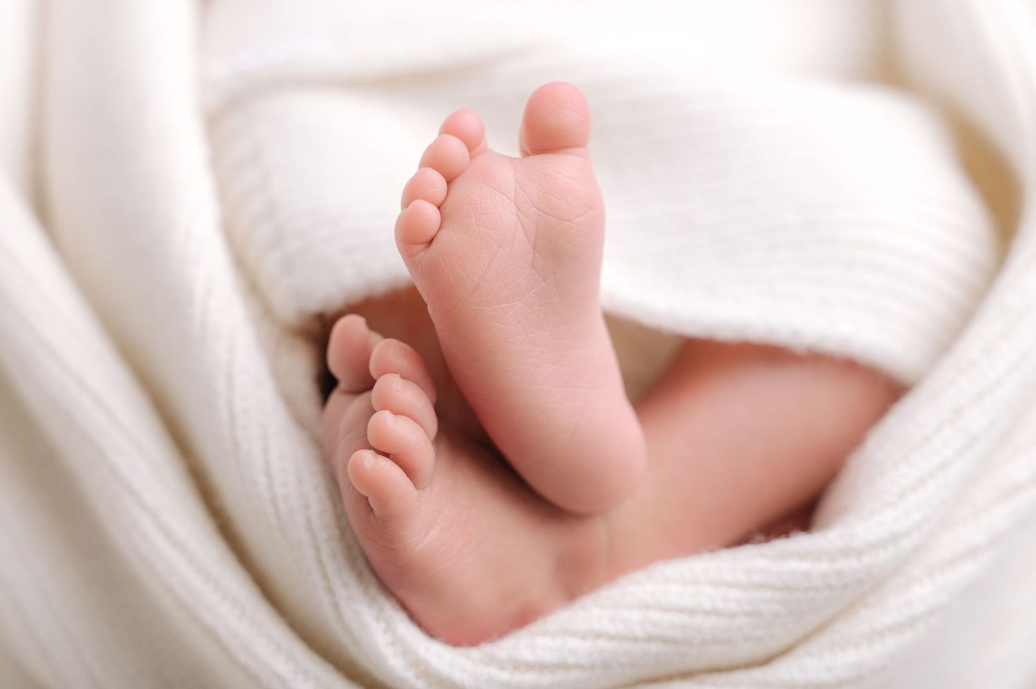Close-up of newborn baby feet wrapped in a soft white knit blanket, perfect for birth announcements.