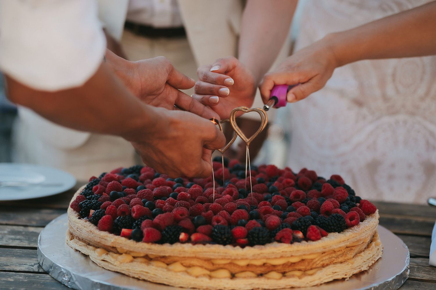 A berry-topped wedding cake being cut on a rustic wooden table.