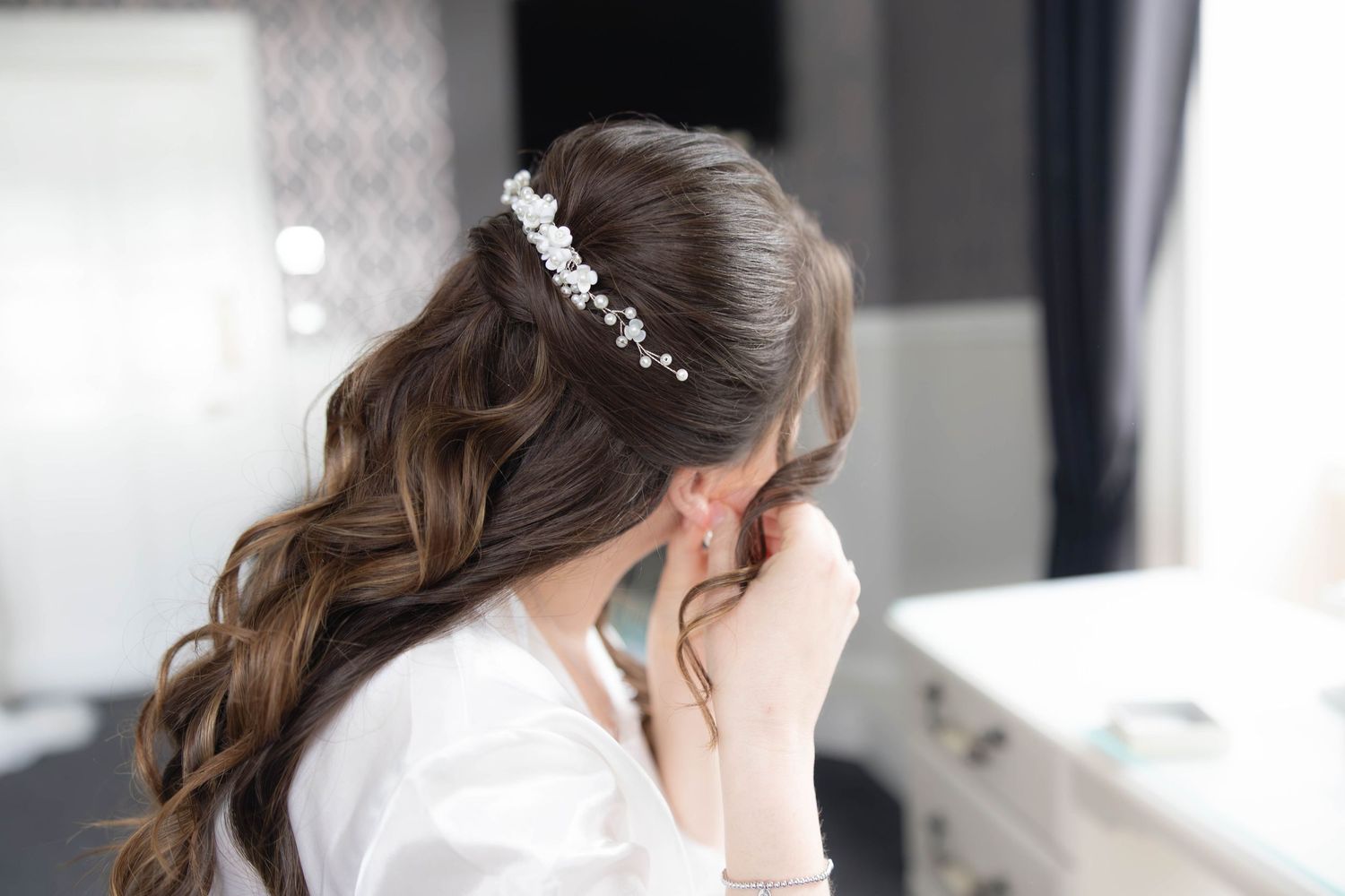 Back view of bride with long dark hair adorned with floral pearl hair comb during bridal preparations.