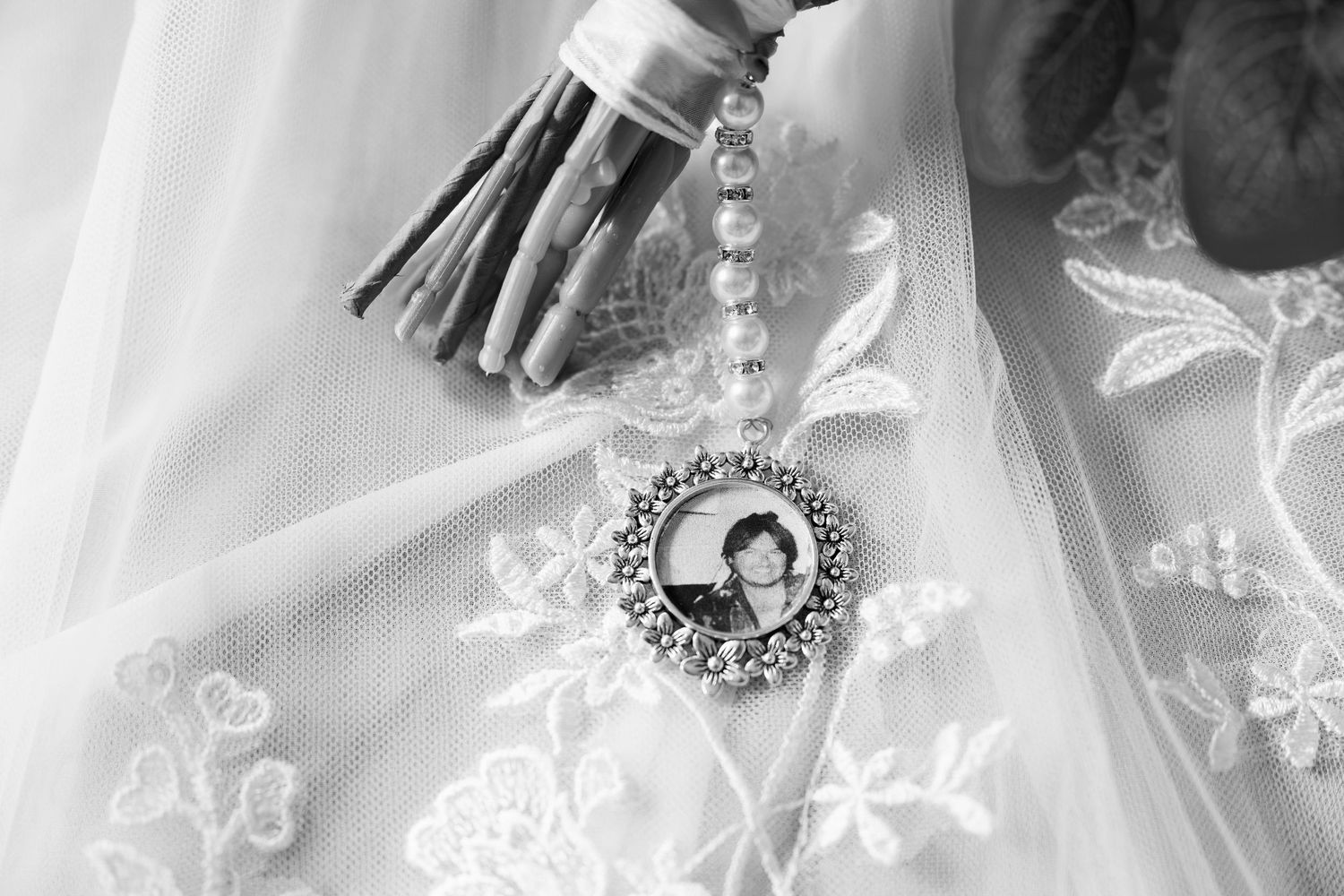 Black and white photo of a bridal bouquet with a pearl charm featuring a memorial portrait photo.