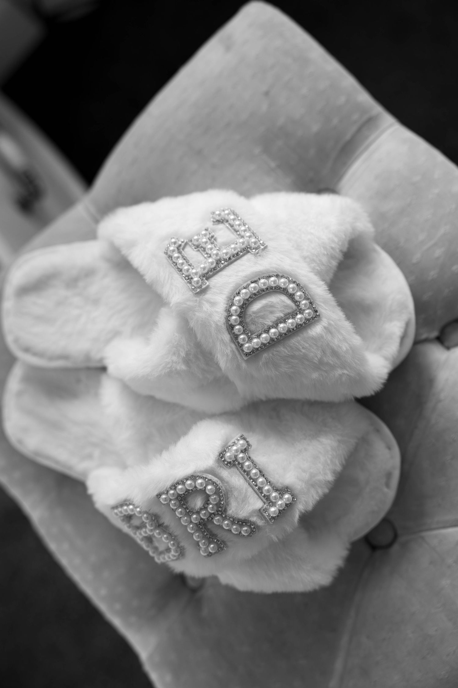 Black and white photo of fluffy white bridal slippers with rhinestone letter embellishments.