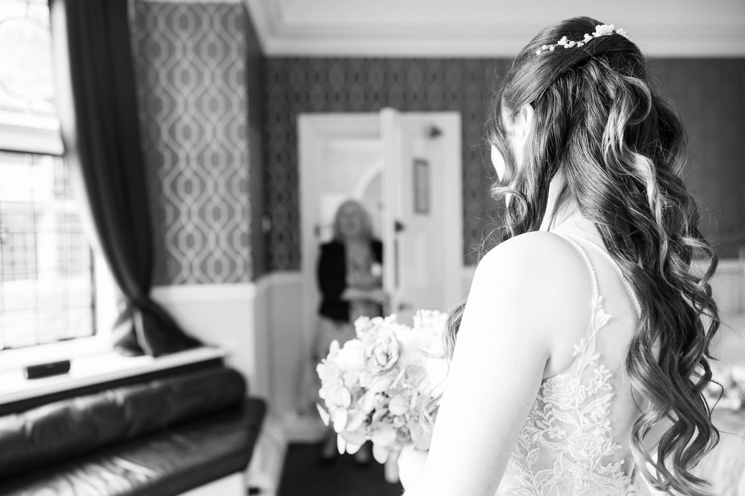 Black and white image of a bride with long curly hair holding a bouquet before her wedding.