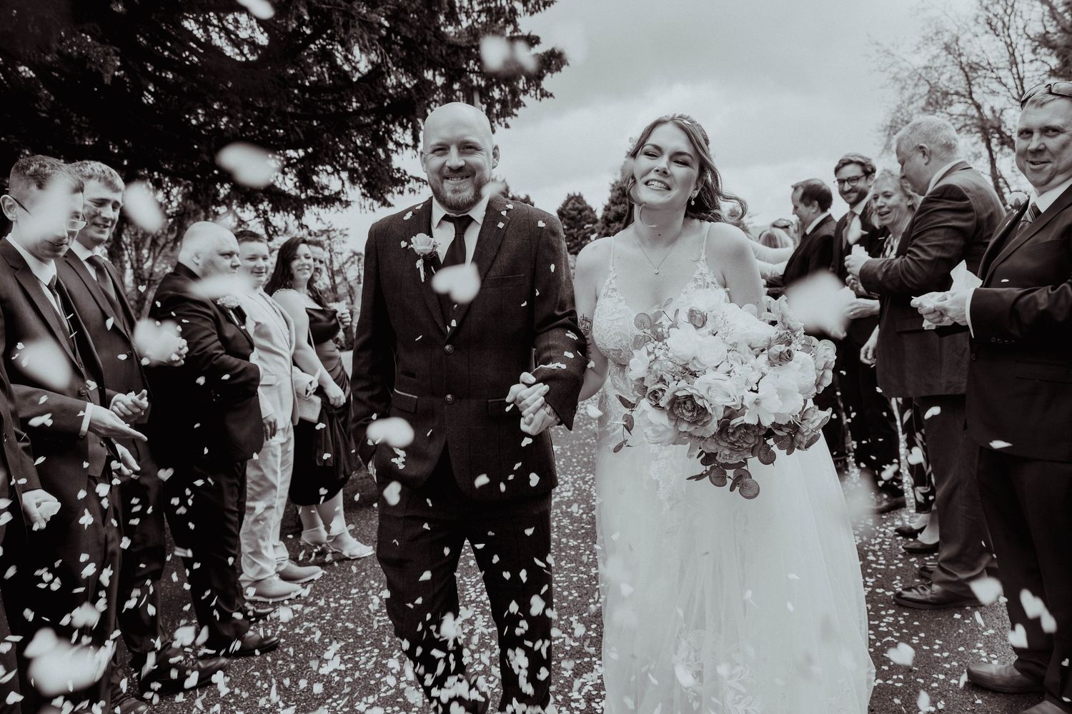 Bride and groom smiling as confetti falls around them in a classic black and white wedding photo. maes manor hotel Blackwood.
