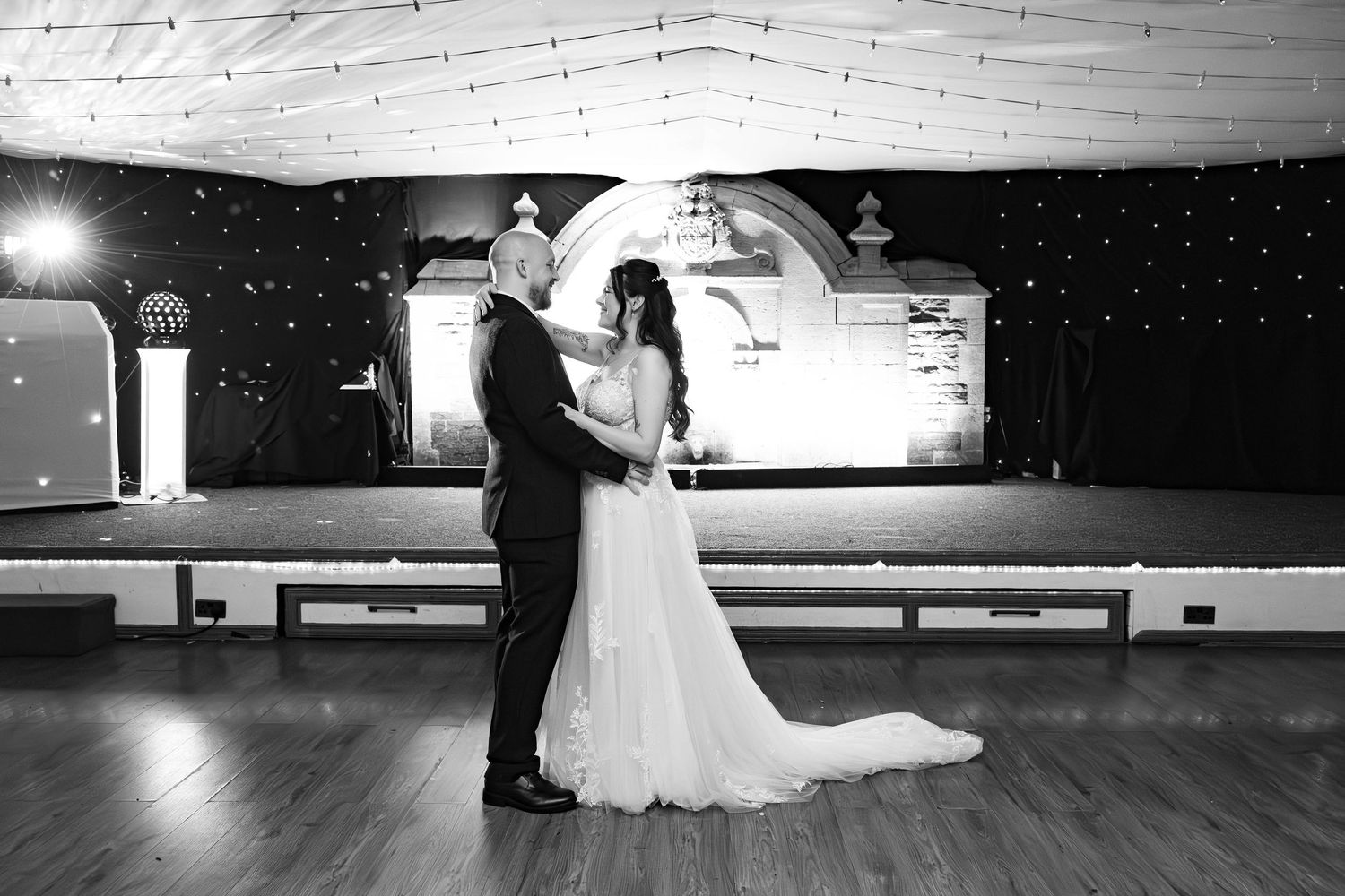 Bride and groom sharing their first dance in a black and white photo in an elegant ballroom.