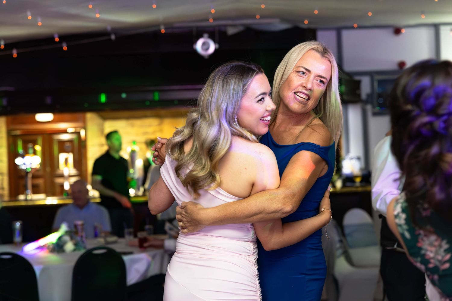 Two women sharing a joyful hug on the dance floor at a lively wedding reception party.