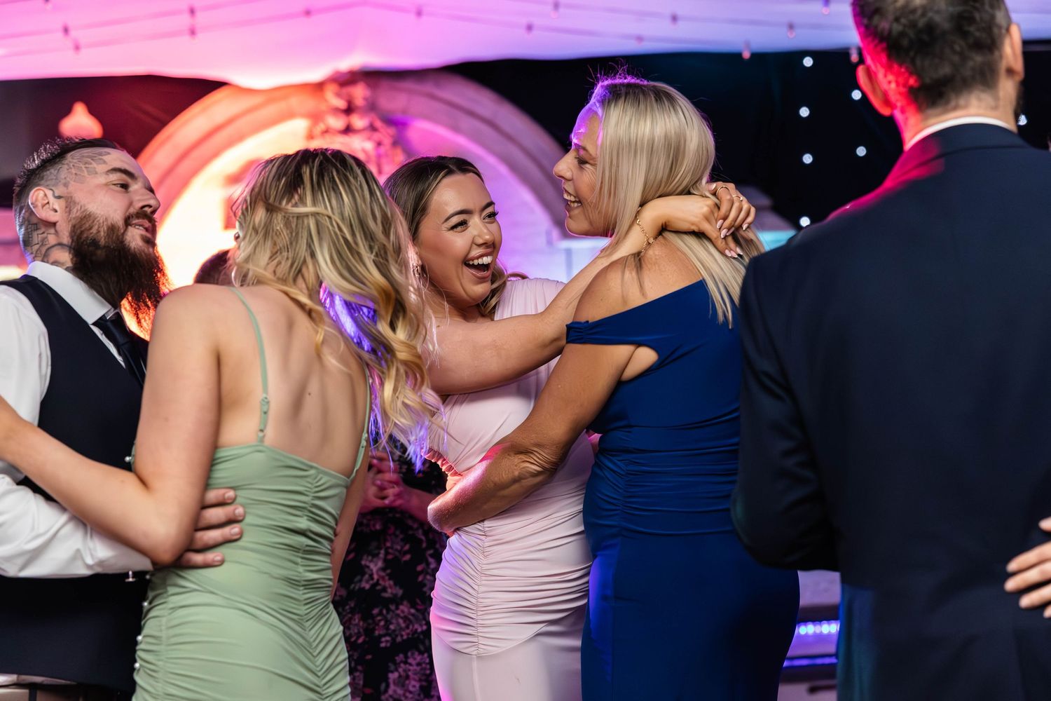 Joyful wedding guests dancing and embracing on the dance floor at a festive evening reception.