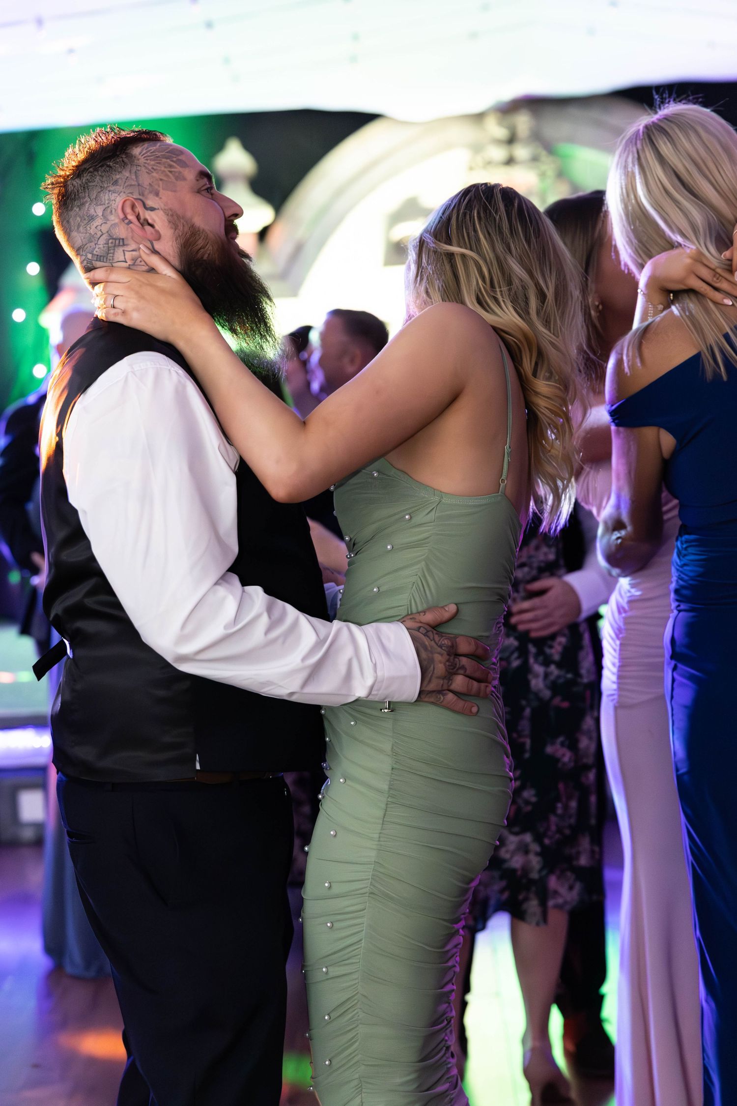 Couple sharing a romantic slow dance at a wedding reception surrounded by other guests.