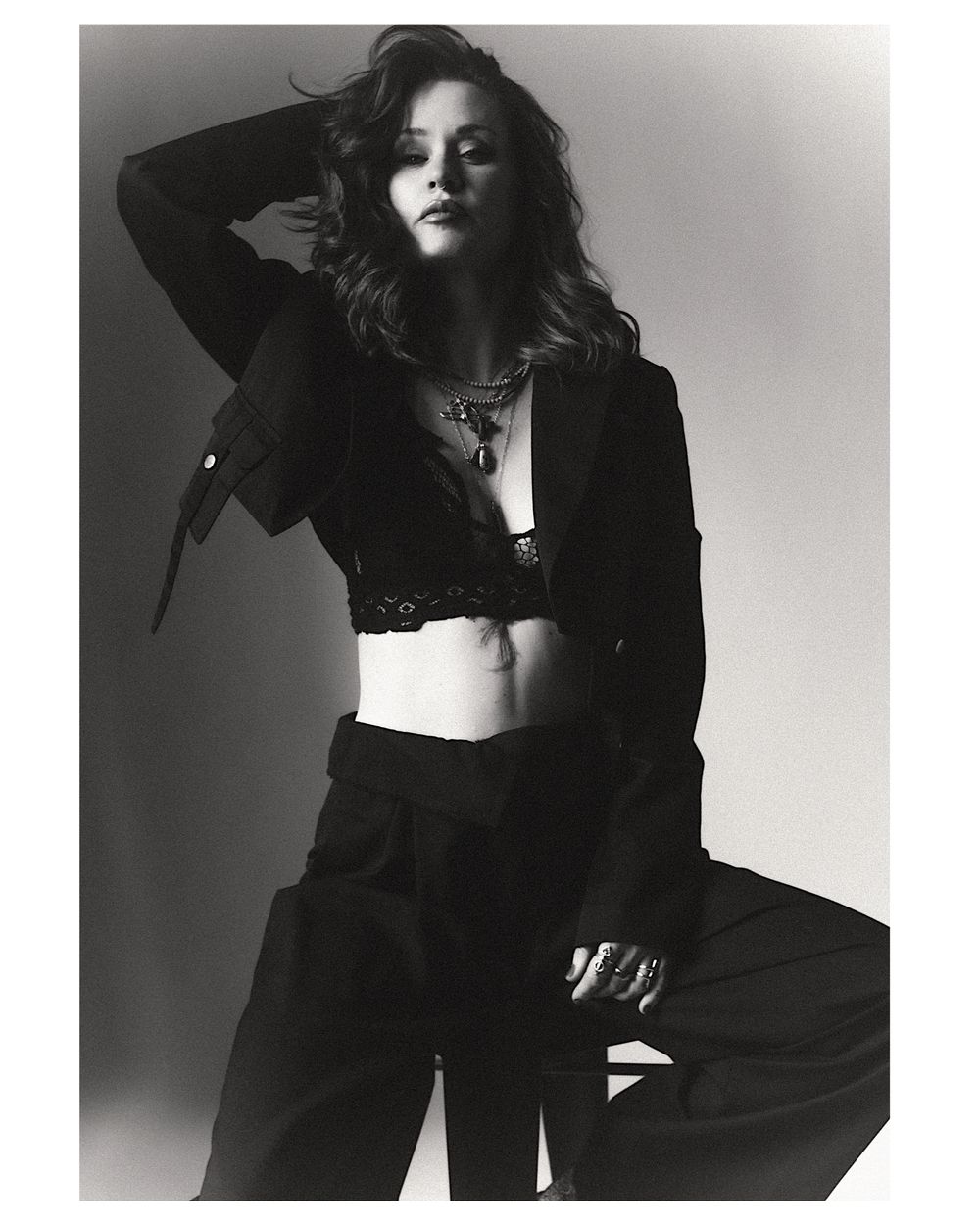Black and white fashion photo of a woman in a blazer, crop top, and wide-leg trousers with layered necklaces.