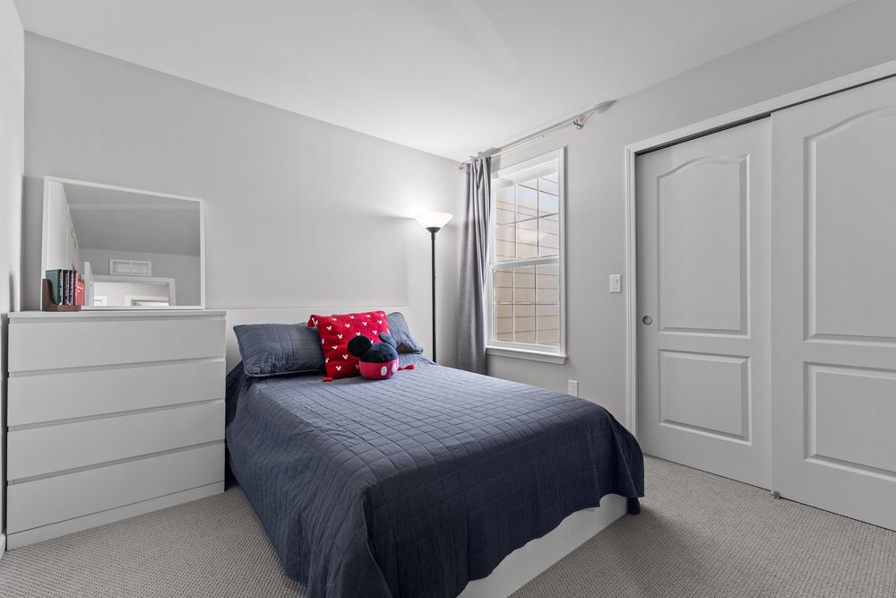 Neutral bedroom with gray bedding, white dresser with mirror, closet with panel doors, and soft natural window light.