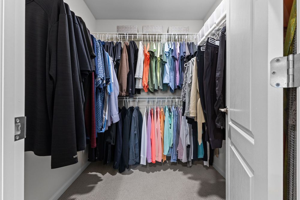 Walk-in closet with double hanging rods filled with organized clothing in various colors on white wire shelving system.