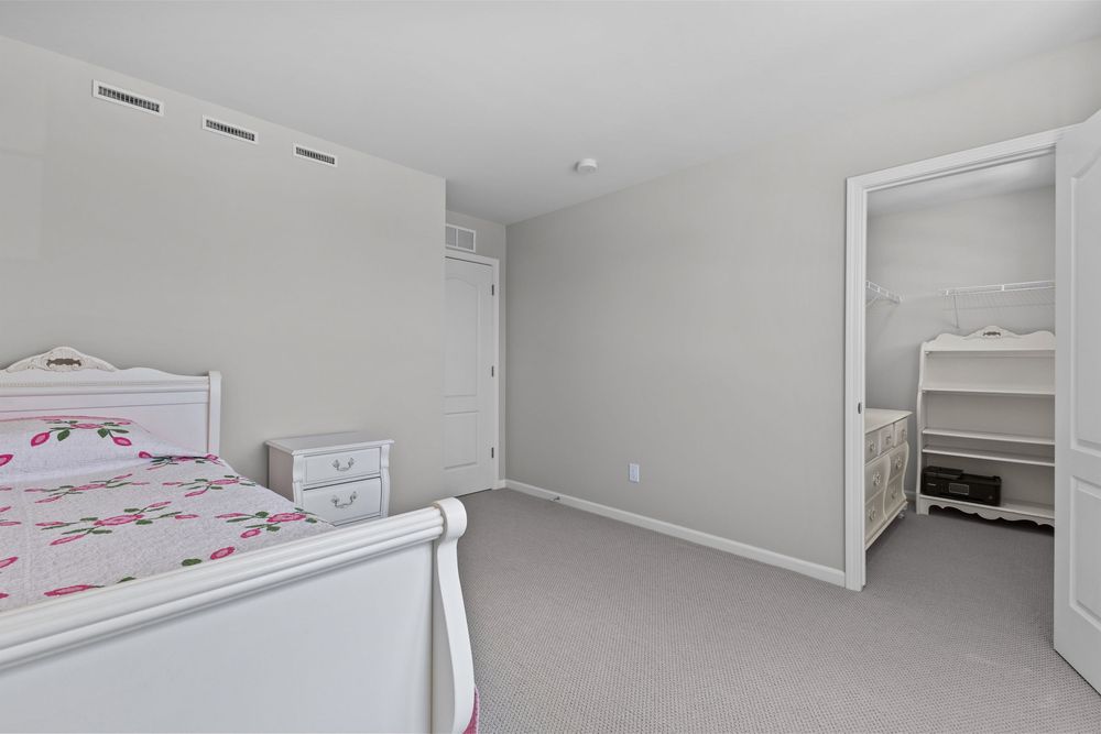 Simple white bedroom with sleigh bed, pink floral bedding, white dresser, and open doorway leading to walk-in closet.