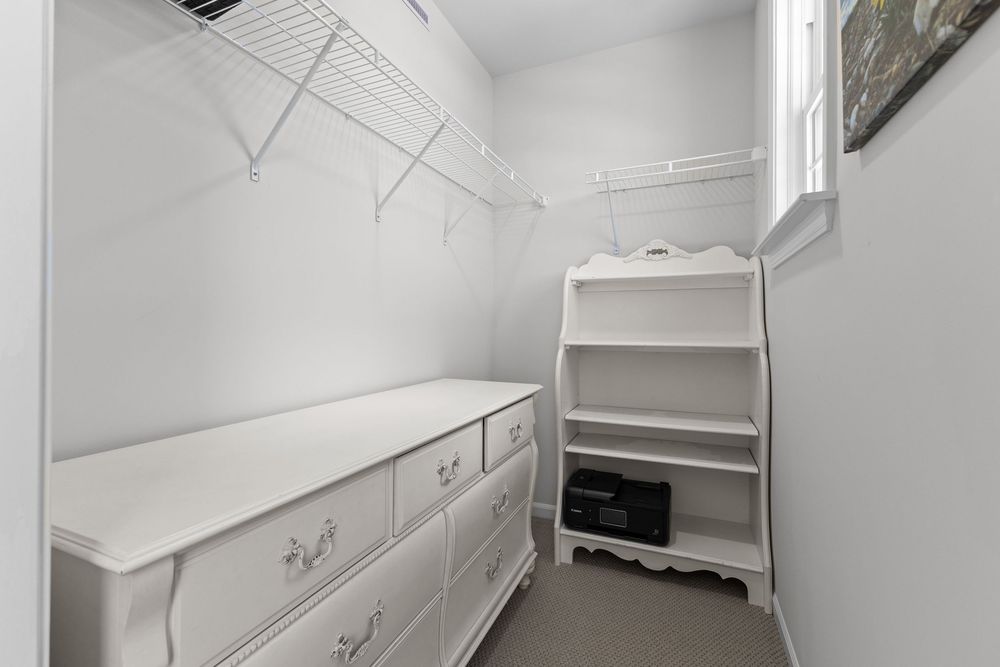 White walk-in closet with wire shelving, built-in dresser with decorative hardware, and open shelving unit for storage.