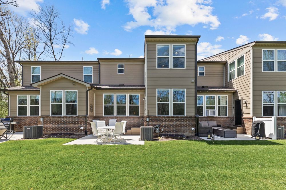 Rear exterior of multi-unit townhomes with brick and siding, patio furniture, and green yard.