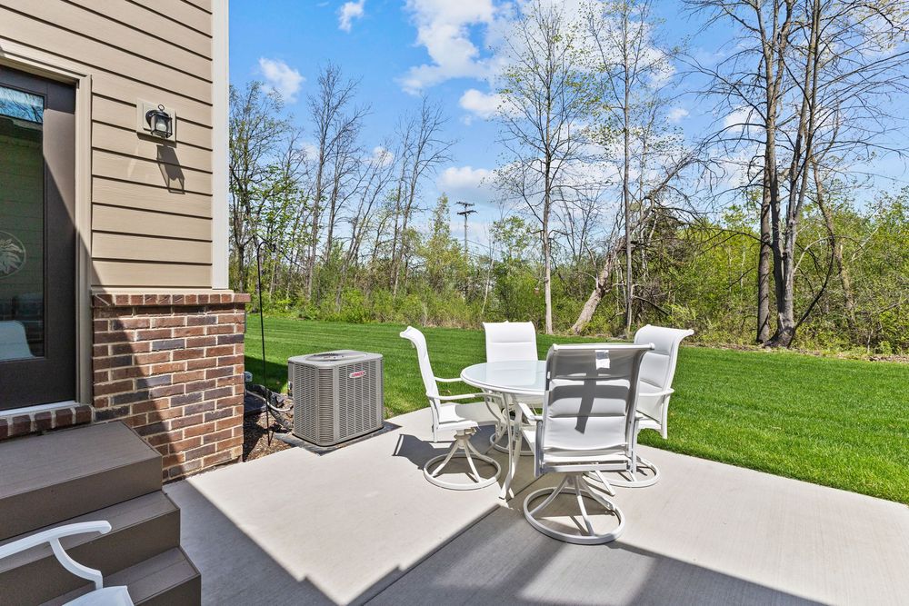 Private concrete patio with white outdoor dining set beside brick townhome and wooded backyard.