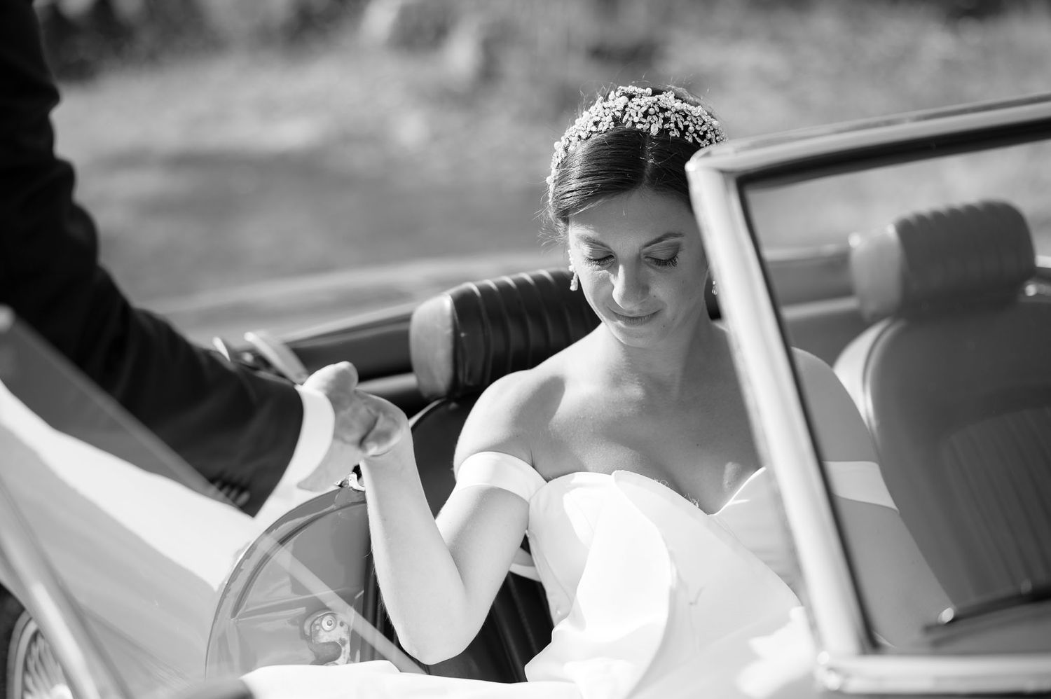 Black and white photo of a bride in a strapless gown stepping out of a vintage convertible car in the garden of Villa Mosconi Bertani