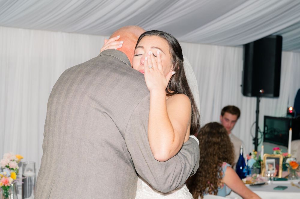 Emotional bride covering her face while embracing groom during first dance at elegant wedding reception.