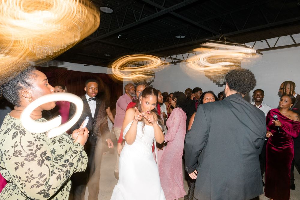 Bride dancing joyfully with guests at a wedding reception, surrounded by swirling light effects.