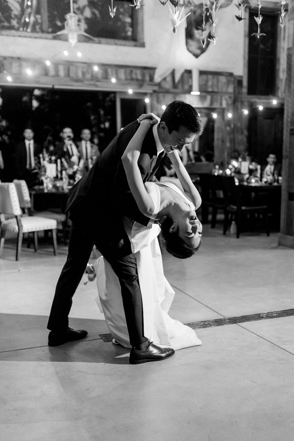 Black and white photo of a groom dipping his bride during their first dance at a wedding reception.