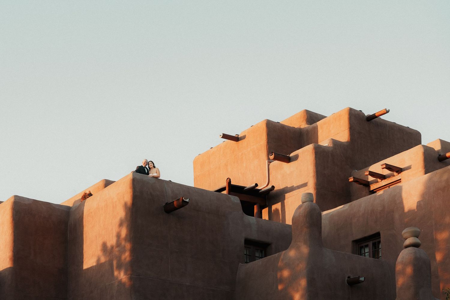 Adobe pueblo-style building with warm terracotta tones and geometric levels against a clear sky at golden hour.