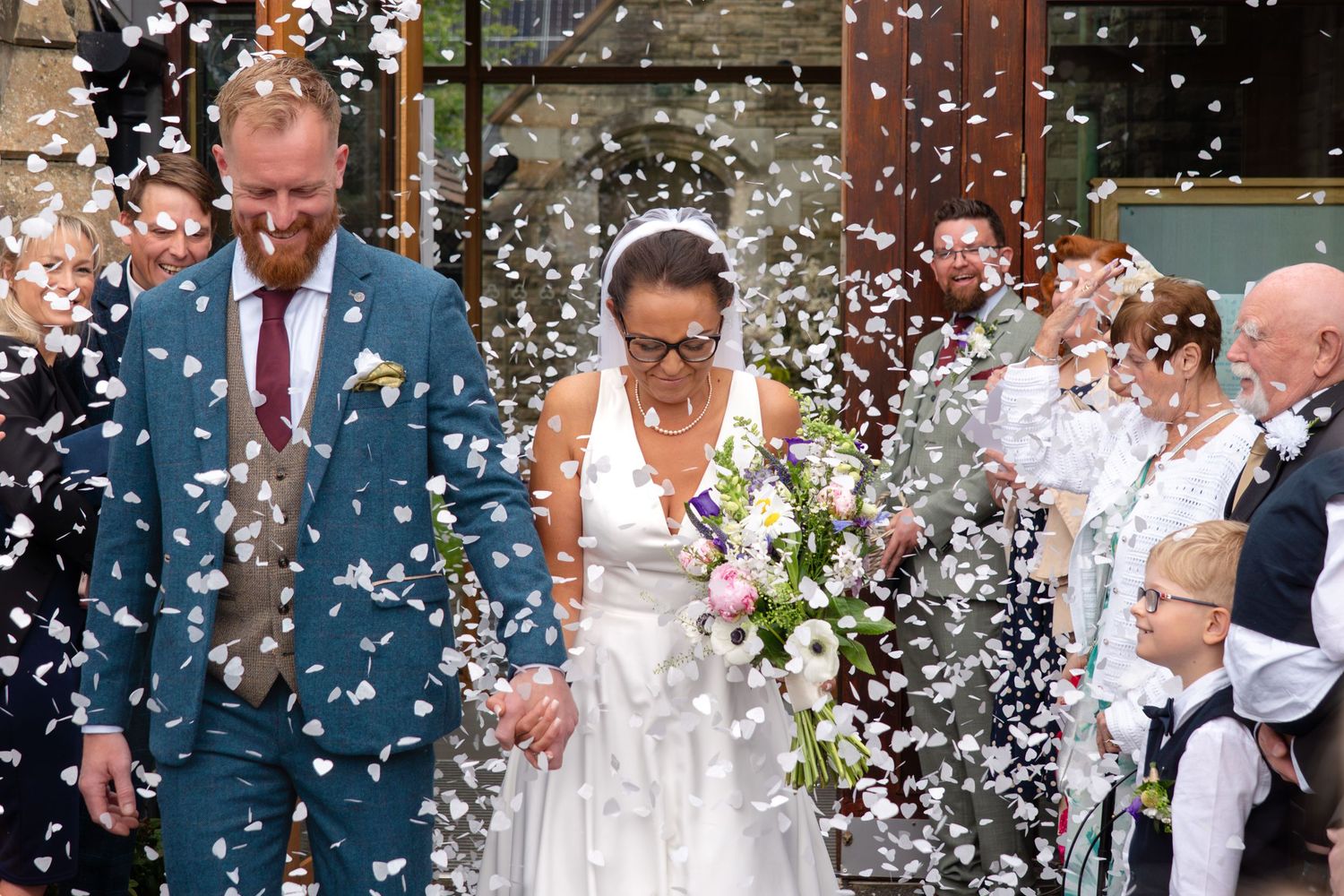 The newly married couple walking out from St Oswald's church in Bollington, while guests shower them in confetti.