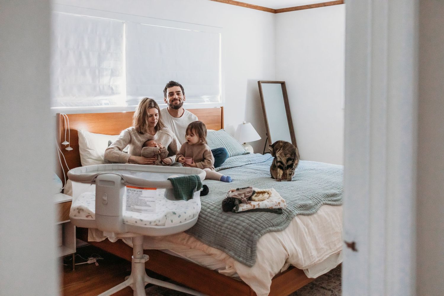 Family of three relaxing on a bed with their dog in a cozy bedroom, sharing a warm moment together.