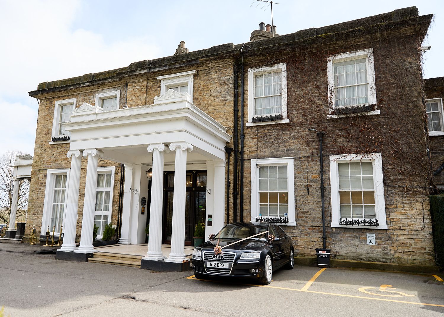 Elegant stone wedding venue Ringwood hall exterior with white columned portico and black wedding car parked outside.