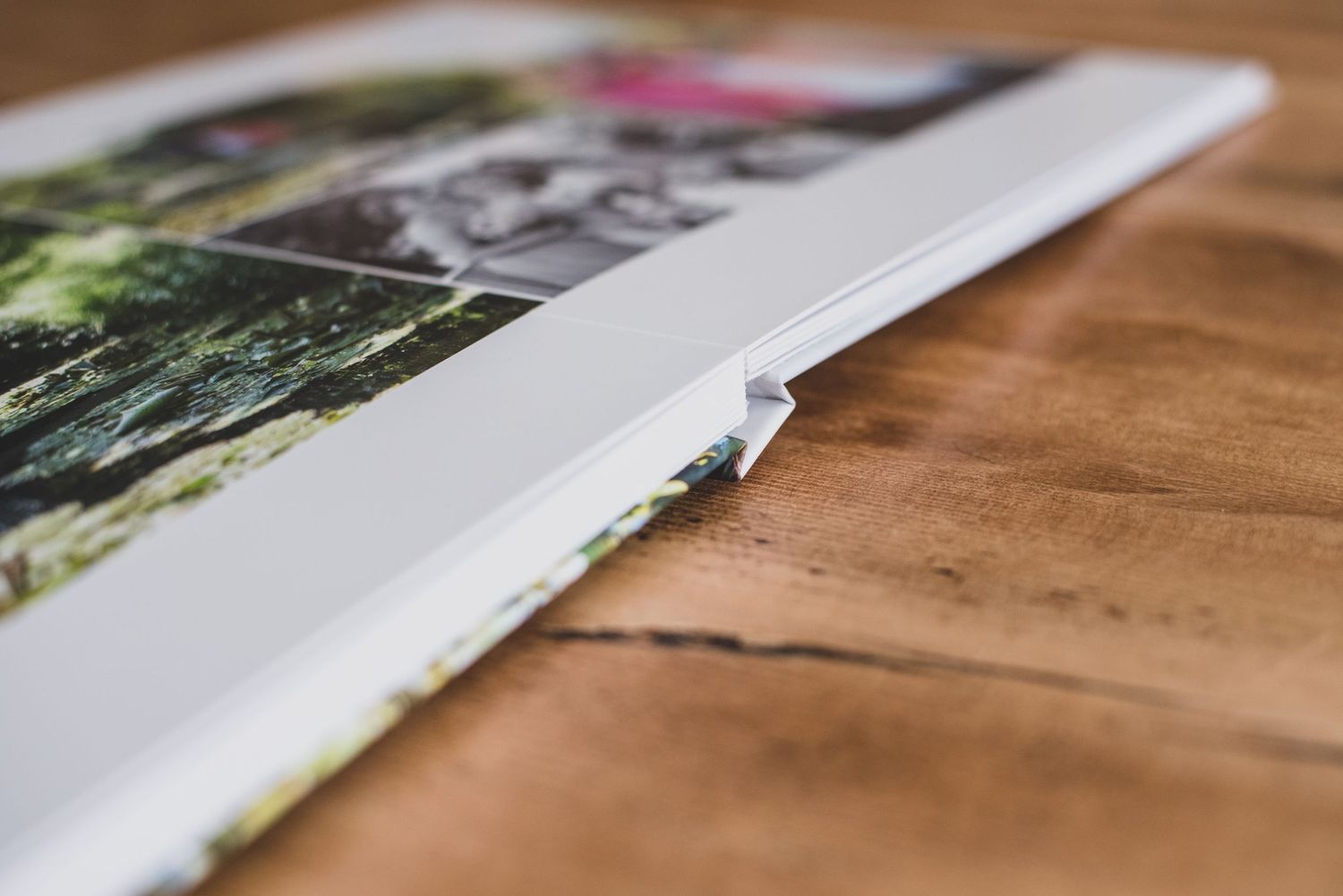 Close-up of a photo album with printed pictures lying open on a wooden table, showcasing its layflat binding.
