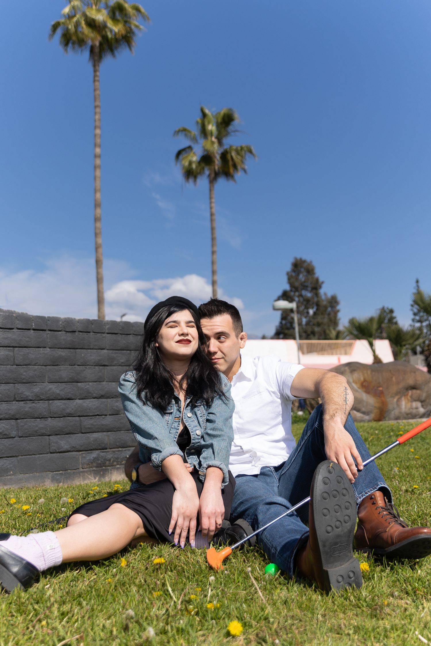 A couple sitting on grass embracing one another during their engagement session while playing mini golf
