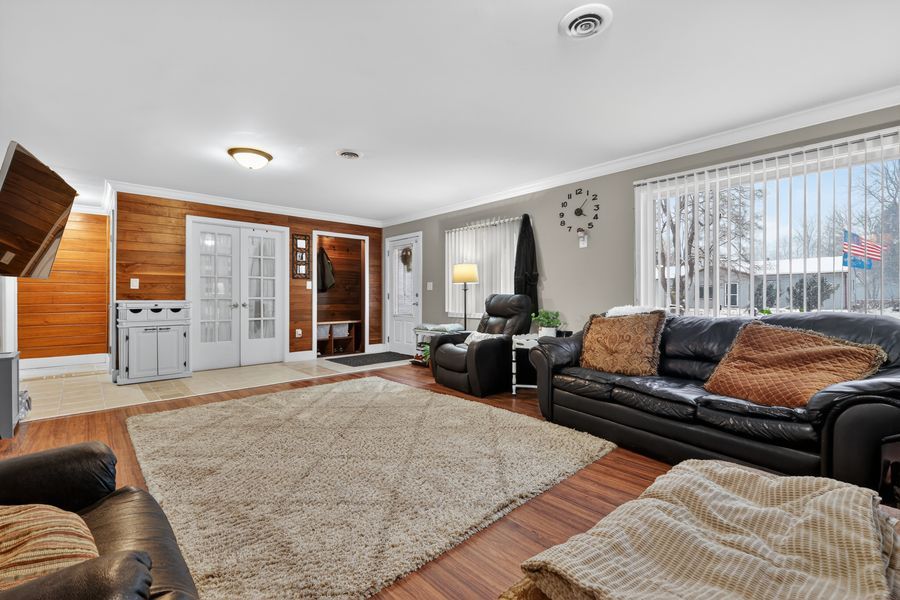 Spacious living room with leather sofas, hardwood floors, large area rug, wood accent wall, and bright windows.