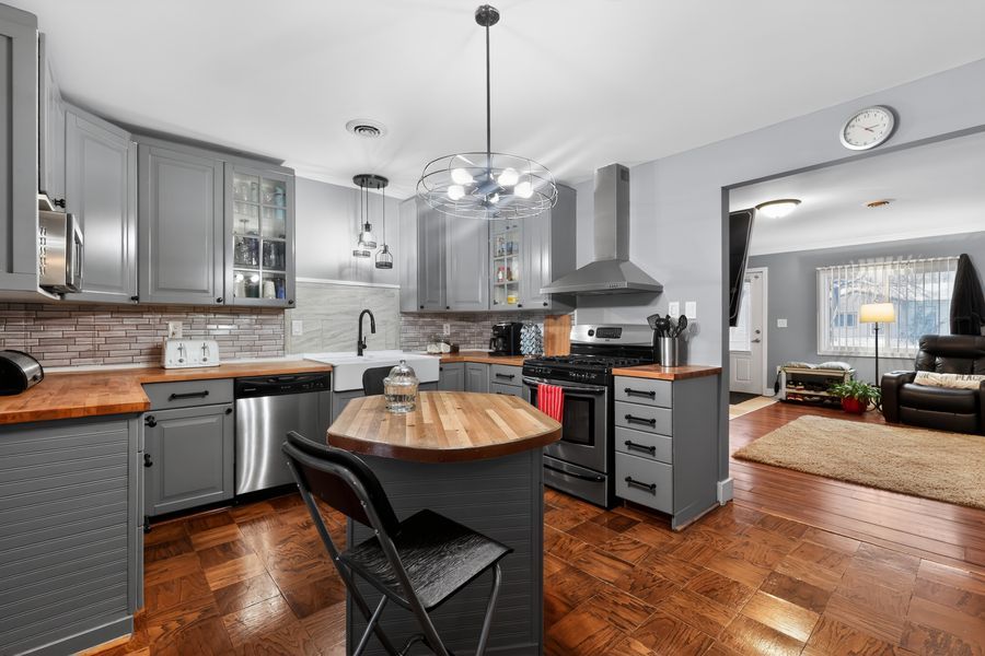 Gray kitchen with butcher block island, brick backsplash, hardwood floors, and stainless steel appliances.