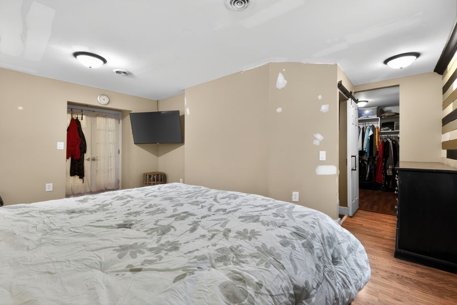 Cozy bedroom with a large bed, hardwood floors, wall-mounted TV, and a walk-in closet visible in the background.