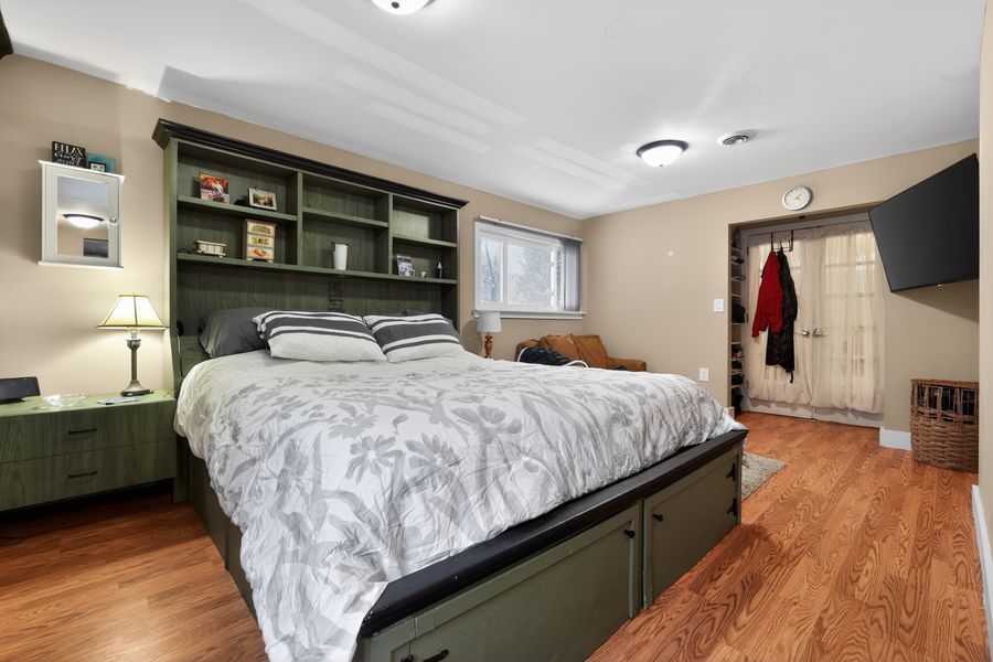 Spacious bedroom with green built-in shelving, king bed with floral bedding, hardwood floors, and a walk-in closet.