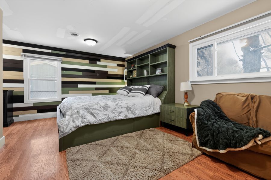 Cozy bedroom with green built-in bookcase headboard, striped accent wall, hardwood floors, and a plush area rug.