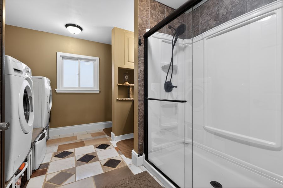 Bathroom with stacked washer and dryer, walk-in shower with glass door, built-in shelving, and diamond-pattern tile flooring.