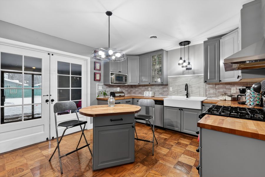 Modern kitchen with gray cabinets, butcher block island, herringbone floors, and chandelier lighting.