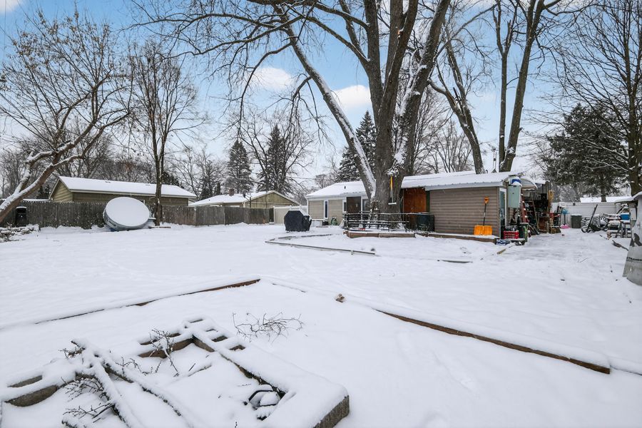 Snow-covered backyard in winter with bare trees, wooden structures, and a shed visible in the background.