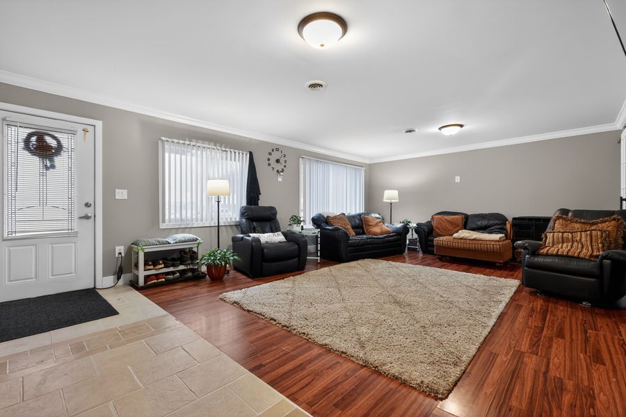 Spacious living room with hardwood floors, large area rug, leather sofas, crown molding, and bright windows near a white front door.