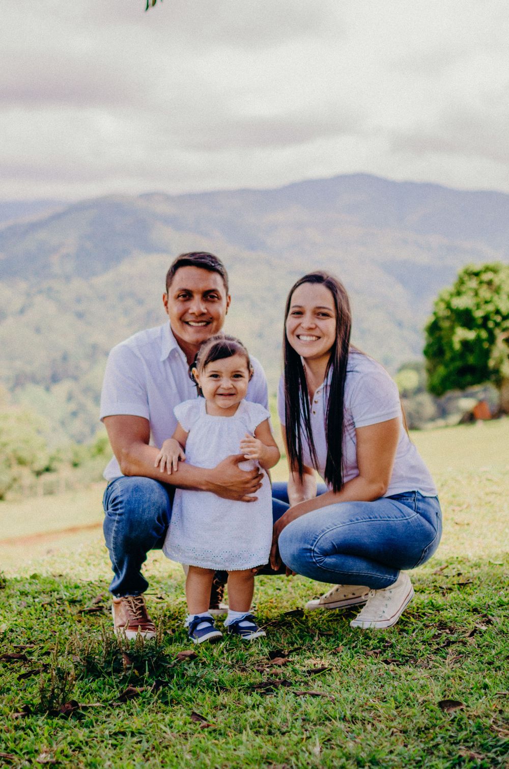 Family kneeling together on grassy hillside with mountains in background.