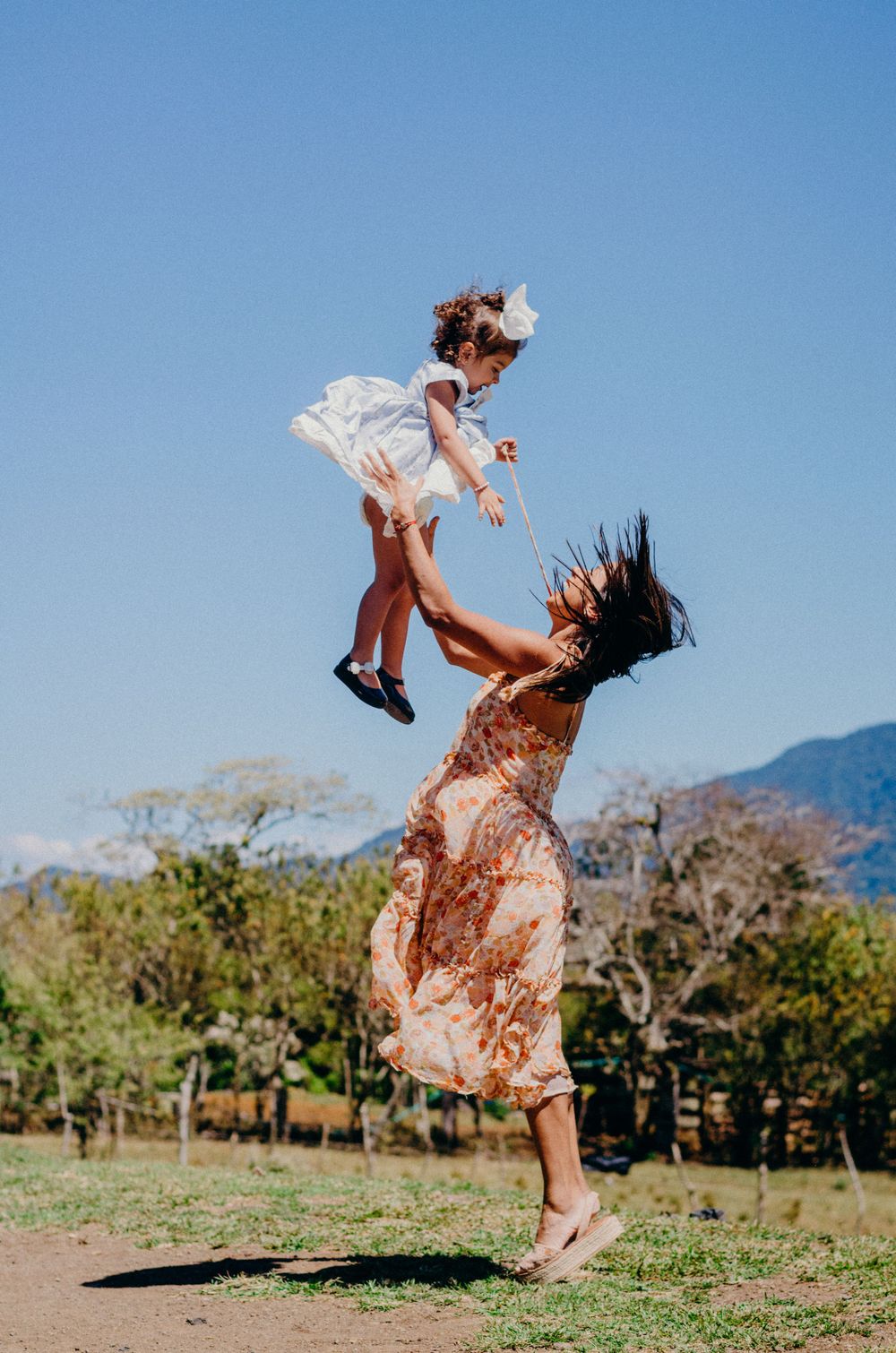 Joyful moment captured as mother tosses child in air against blue sky.