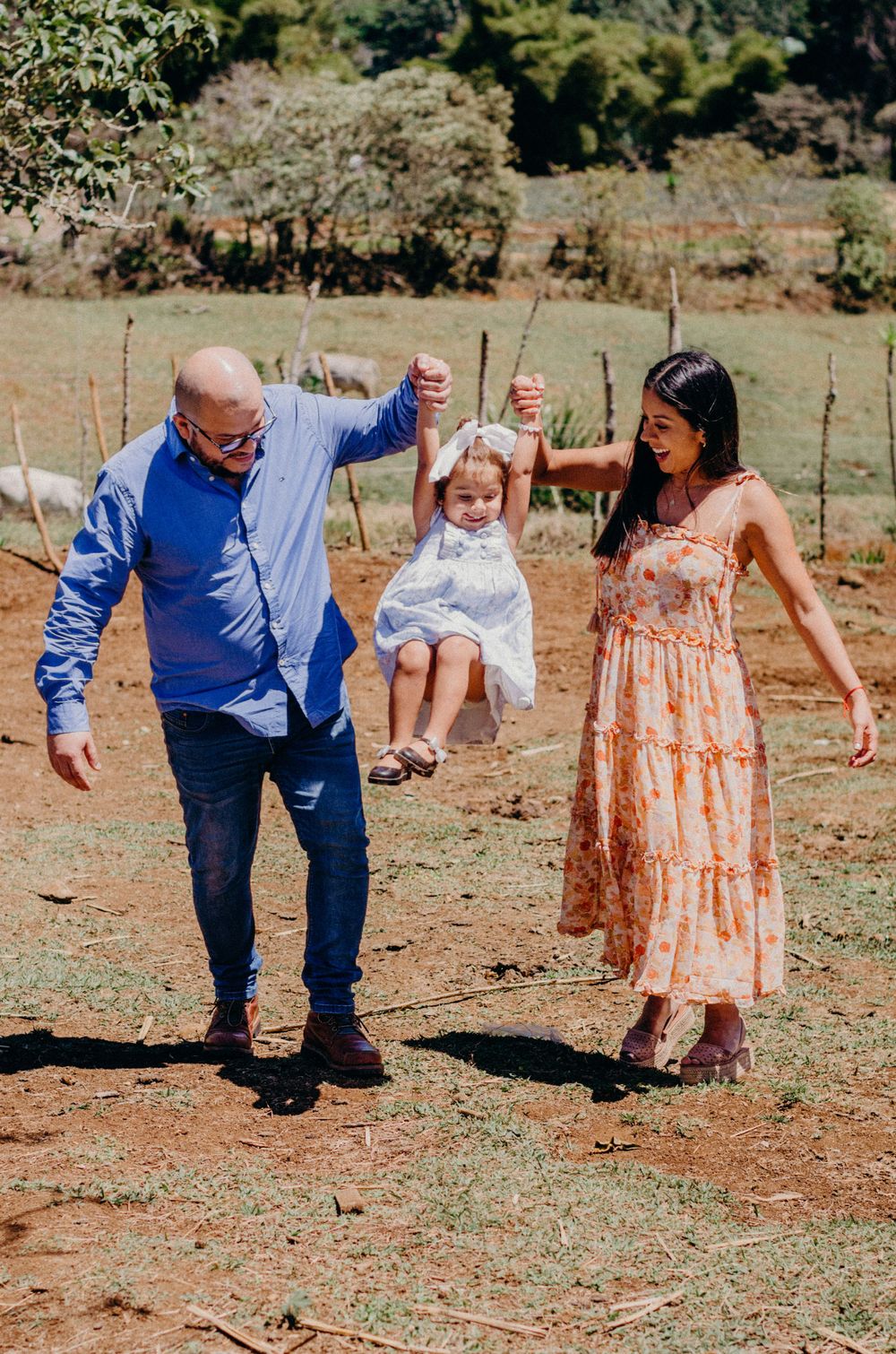 Parents swing child together in outdoor countryside setting.