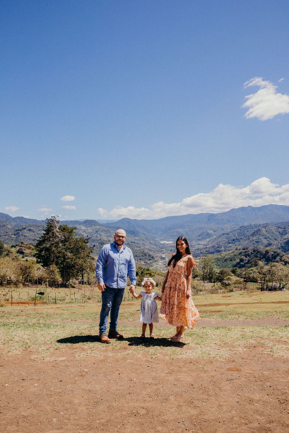 Family standing together on dirt path with mountain landscape behind them.