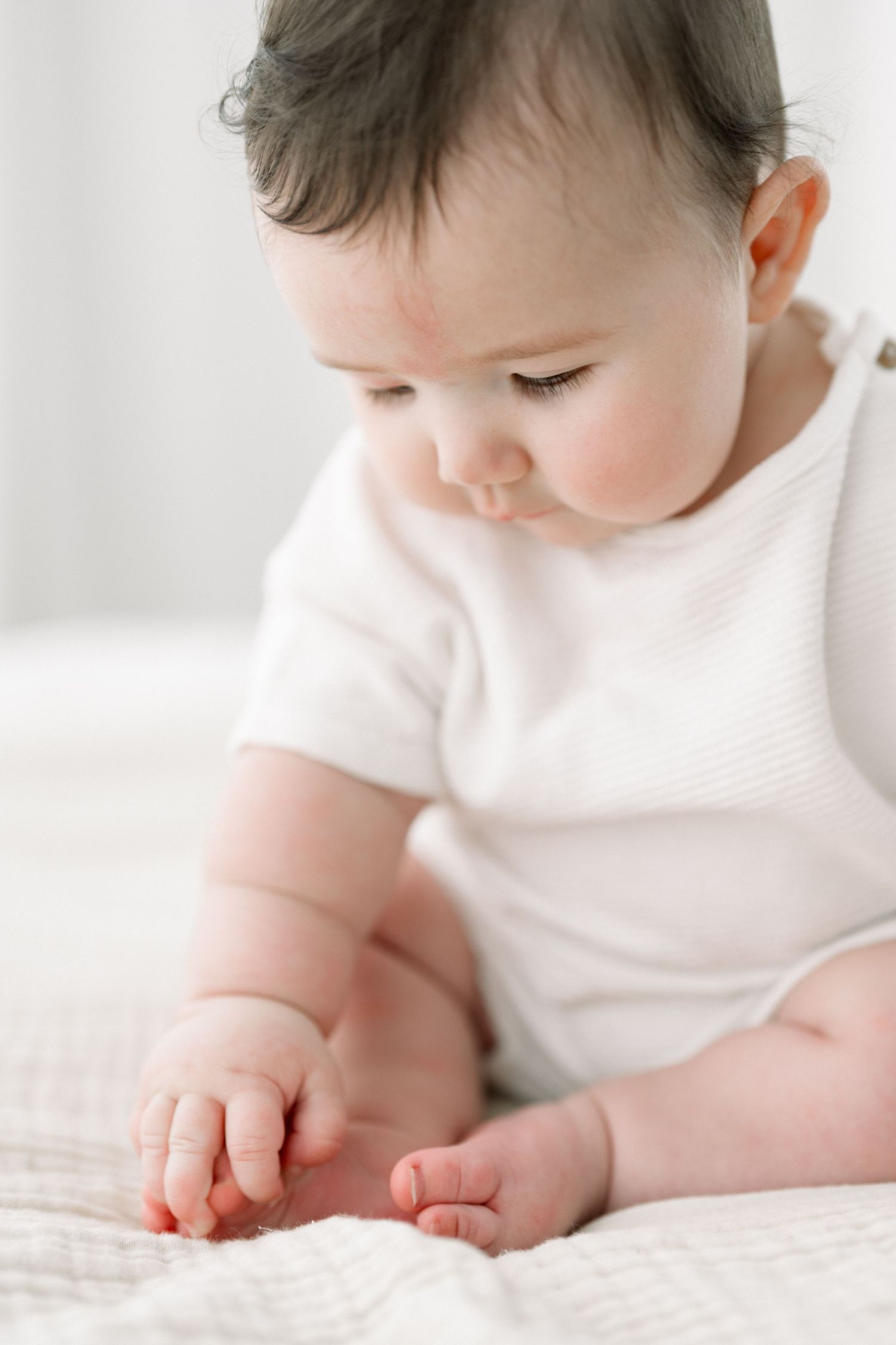 Bébé de 6 mois assis et explorant ses orteils lors d’une séance photo bébé 3-12 mois au studio photo lumineux près de Québec