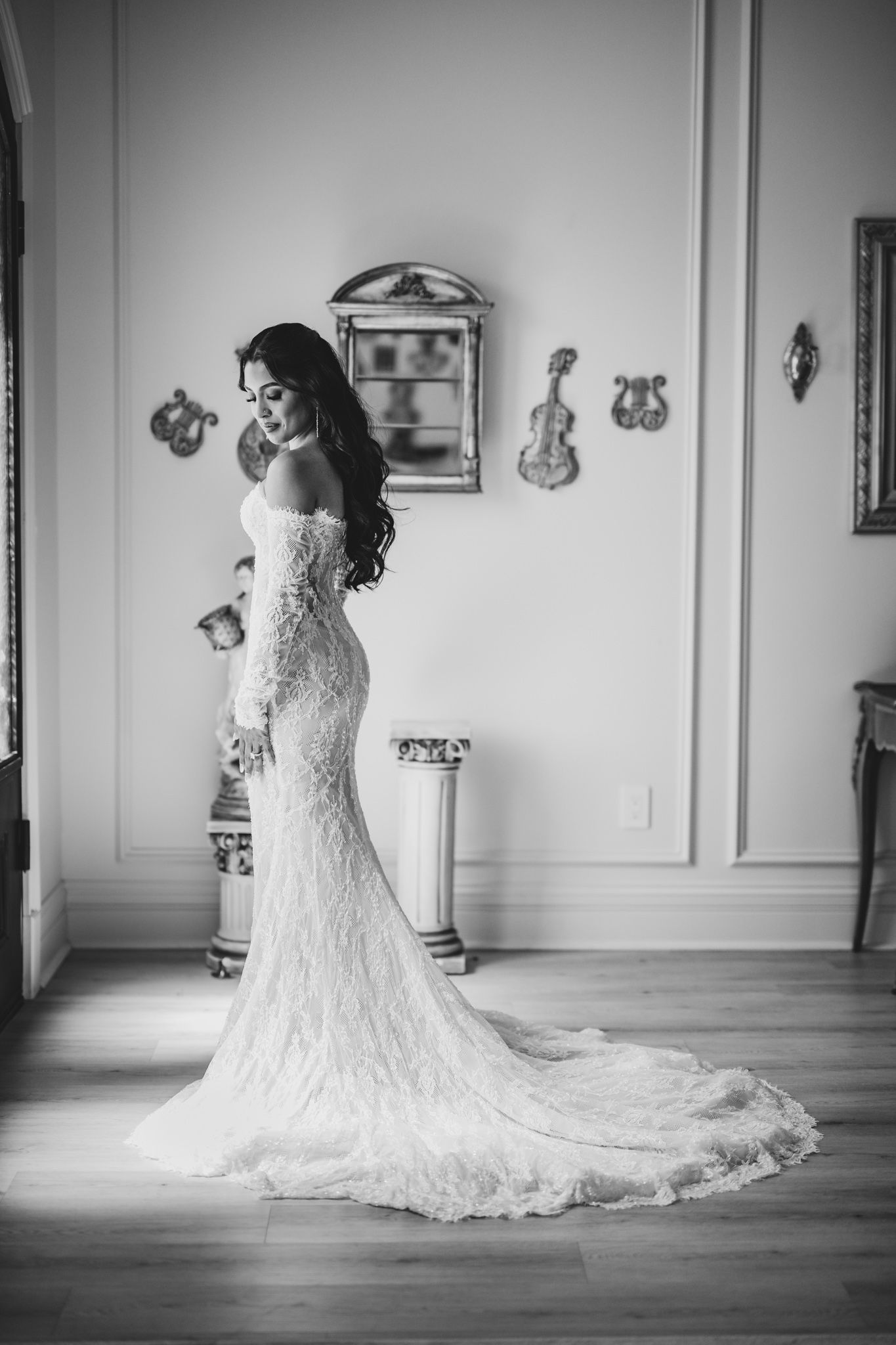Bride in elegant lace mermaid wedding gown with train poses in black and white portrait in ornate room.