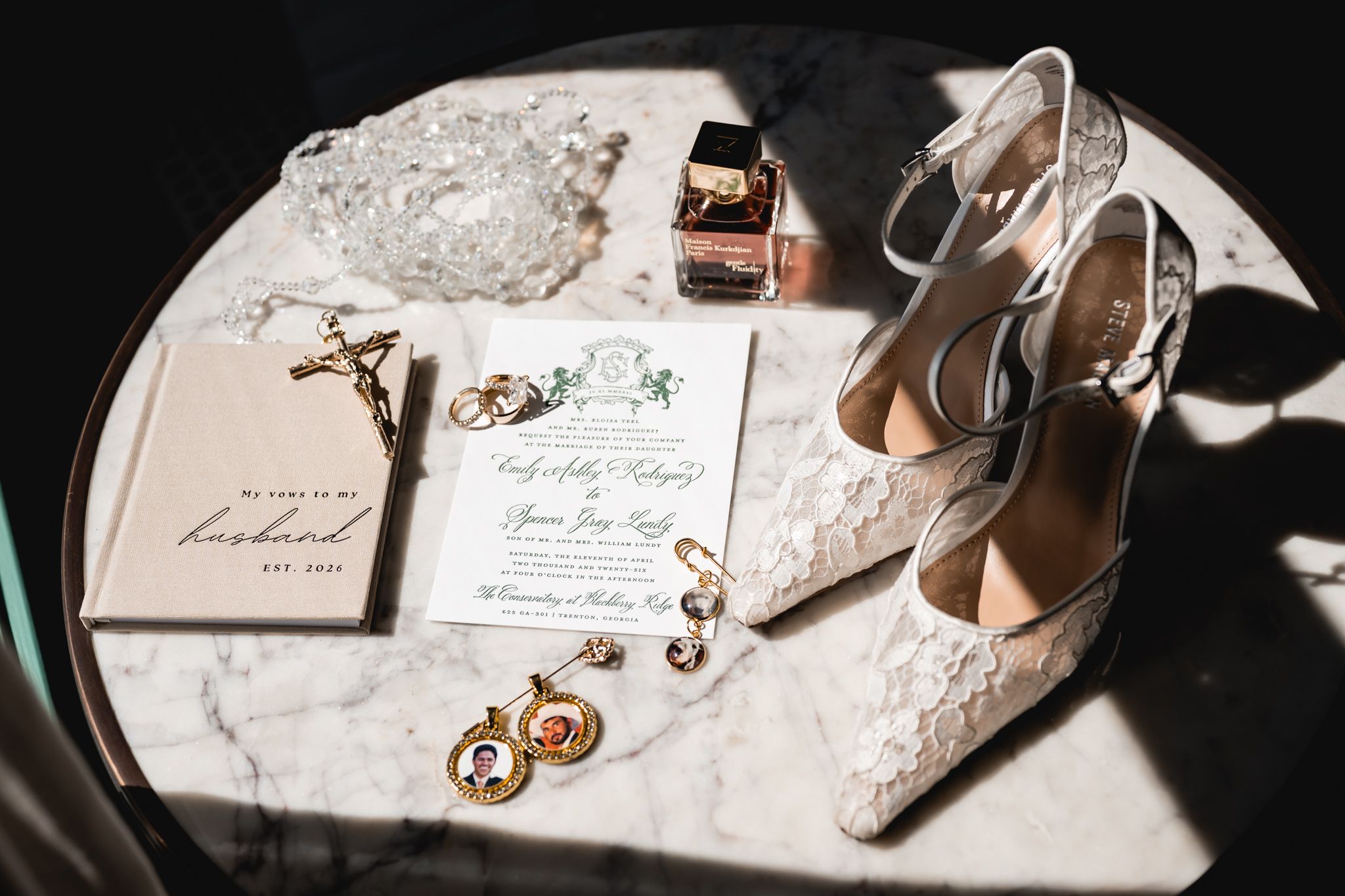 Elegant wedding flat lay with lace heels, gold earrings, floral invitation, perfume, and a sentimental book on marble table.