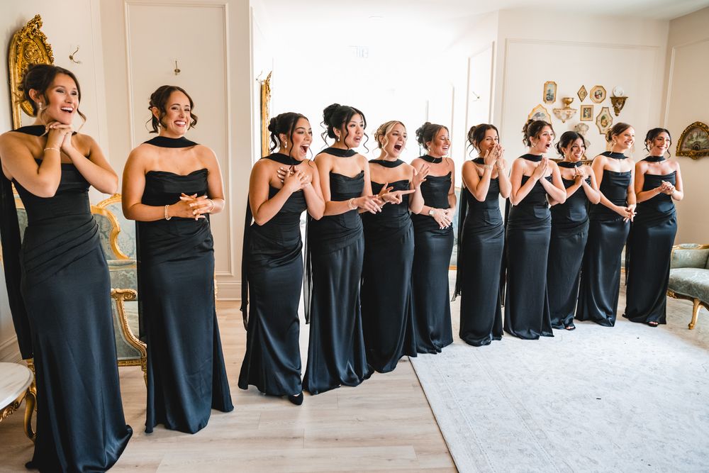 Bridesmaids in matching black gowns posing together in a bright wedding venue room.
