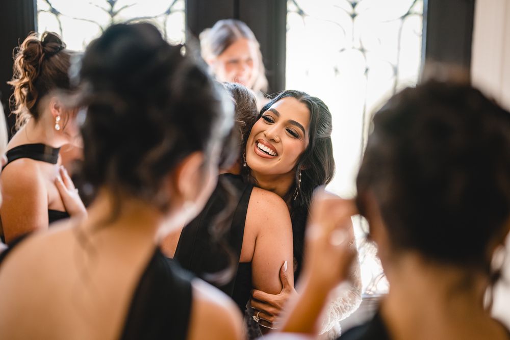 Bride in black dress laughing joyfully while embracing guests at wedding celebration.