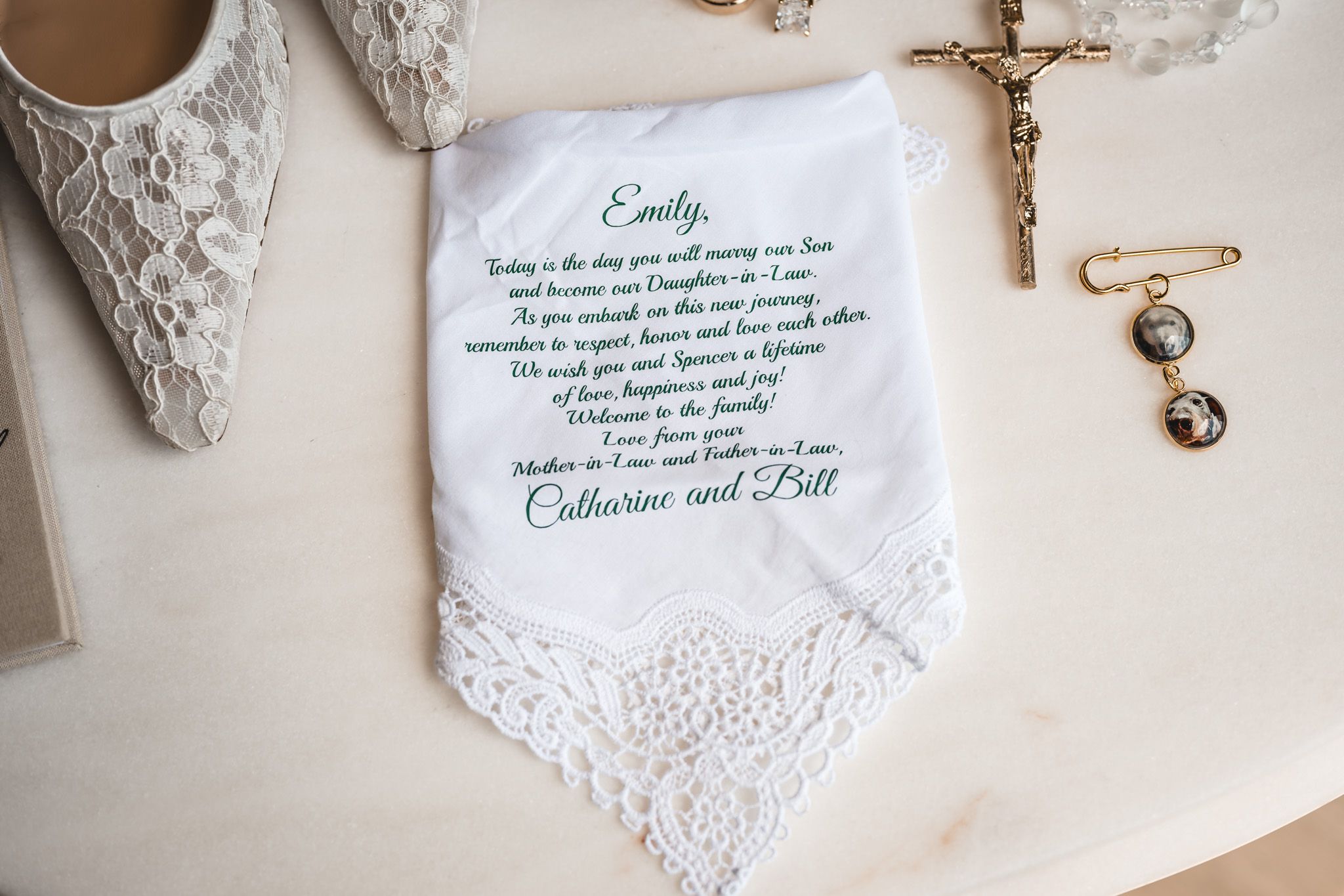 Personalized wedding handkerchief with green script message from parents, displayed beside bridal shoes and gold rosary.